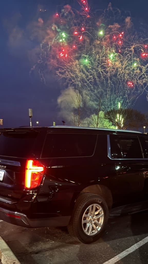 Luxury black SUV at a corporate celebration with fireworks in the background